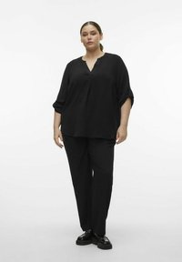 Svart, texturerad blus med V-ringning och trekvartsärmar, kombinerad med svarta byxor och platåskor, vilket skapar en monokrom look.