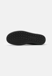 Schwarze Schuhsohle aus strukturiertem Gummi mit kreisförmigen Mustern für besseren Grip, leicht gebogene Form und glatte Kanten.