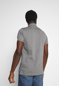 Grå pikétröja med korta ärmar, med en klassisk krage och sidslitsar, bärs med blå jeans. Slät textur och kroppsnära design.