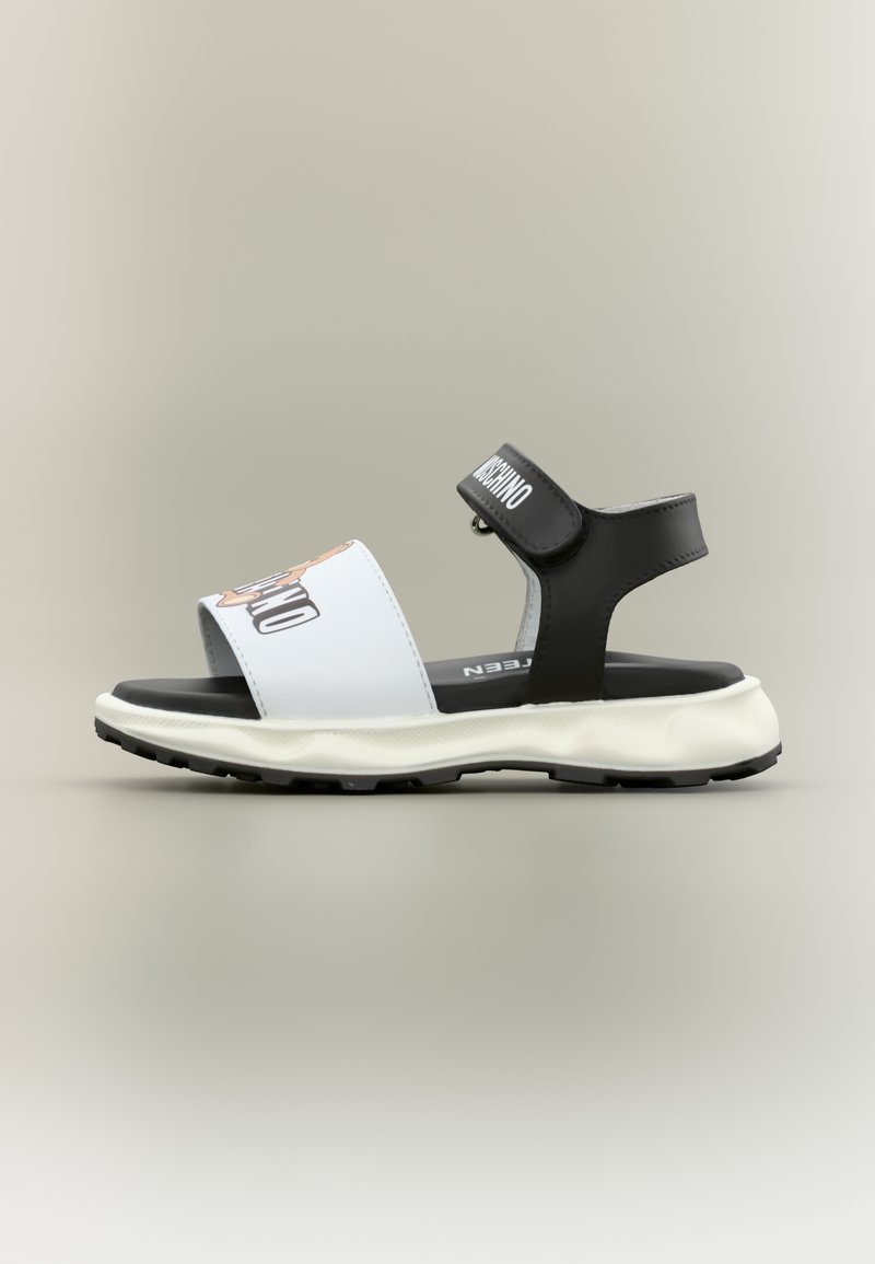 Μαύρο και άσπρο σανδάλι με παχιά σόλα, ρυθμιζόμενο λουράκι στον αστράγαλο και λουράκι μπροστά με γραφικό καφέ αρκούδας και κείμενο επωνυμίας.