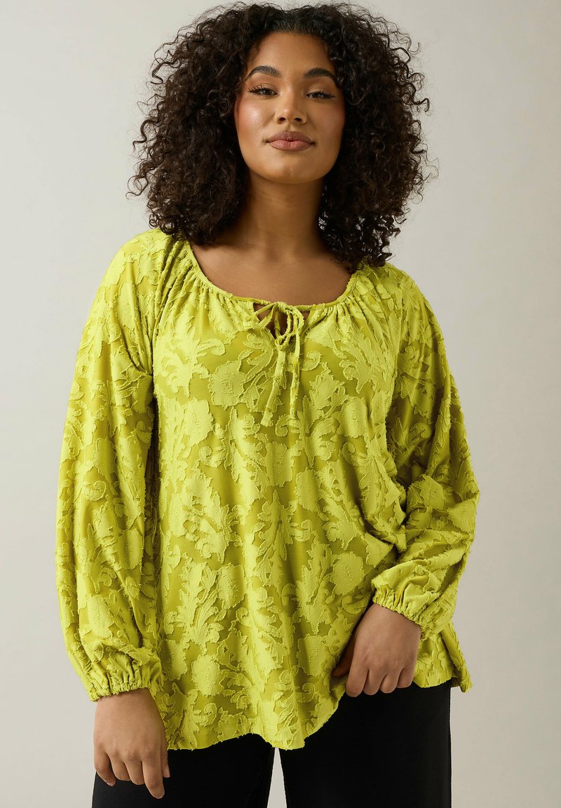 Långärmad, ljusgul blus med blommönster, rundad halsringning och dragsko-detalj, avslappnad passform, elastiska ärmslut.