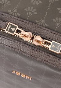 Grå handväska med en texturerad yta, som har ett blommotiv. Detaljer i guldfärgad dragkedja och varumärke är synliga.