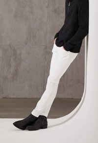 Suéter negro de punto, pantalones ajustados blancos y botas de tobillo de cuero negro con cremallera lateral. Texturas suaves, corte moderno y colores en contraste.