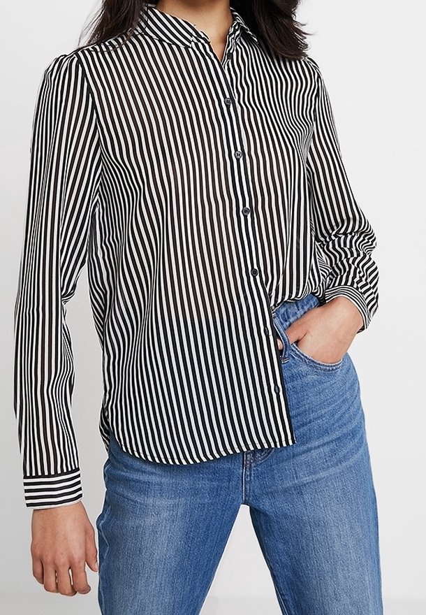Skjorte med krave og knapper i sort og hvide lodrette striber, lange ærmer og slank pasform; kombineret med blå jeans.