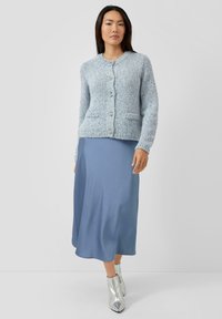 Jasnoniebieski dziany kardigan z srebrnymi guzikami, z dwoma przednimi kieszeniami. W połączeniu z niebieską, satynową spódnicą sięgającą kolan oraz srebrnymi botkami na kostkę.
