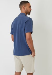 Navy poloshirt voor heren met een kraagdesign, korte mouwen en een gladde textuur, gecombineerd met lichtbeige shorts.