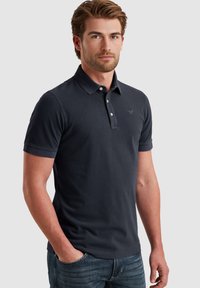 Polo majica tamnoplave boje od pamuka, s ovratnikom, tri dugmeta, kratkim rukavima i suptilno vezenom logotipom na prsima.