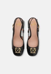 Chaussures slingback en cuir verni noir avec un bout rond, détail du logo "M" en or, et une sangle réglable. L'intérieur est doté d'une doublure beige clair.