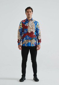 Chemise à boutons multicolore avec motifs floraux et léopard, présentant des couleurs bleue, rouge et beige. Manches longues, conception à col.