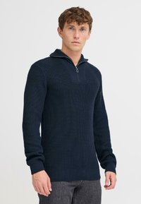 Navy knit sweater with a zip-up collar, ribbed texture, and long sleeves. Features a textured pattern and fitted cuffs at the wrists.