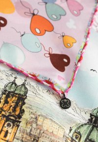 Kleurvolle zijden sjaal met een design van pastelballonnen en harten, omzoomd met een roze rand en versierd met een decoratieve bedel. Platterzicht.