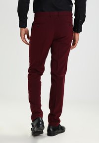Burgundi színű, slim fit szabású nadrág, hátsó zsebekkel, fekete öltönyi cipővel és fekete hosszú ujjú inggel párosítva.