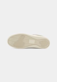 Semelle d'une basket beige clair avec des motifs de bande de roulement en zigzag et circulaires et une section rectangulaire avec logo dans la zone de la voûte plantaire.