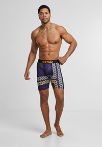 Čierne a zlaté boxerky s logom na páse, s dizajnom pneumatiky v purpurovej a šedej farbe, vyrobené z elastického materiálu pre pohodlie a dobré sedenie.