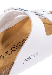 Sandalia blanca con plantilla de corcho, que cuenta con una correa de cuero suave, herrajes plateados y el nombre de la marca "palado" impreso en negro.