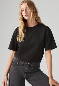 Tricou scurt negru cu mânecă scurtă, cu guler rotund, fabricat din bumbac, purtat cu blugi de denim gri închis cu talie înaltă, cu accente de cupru.