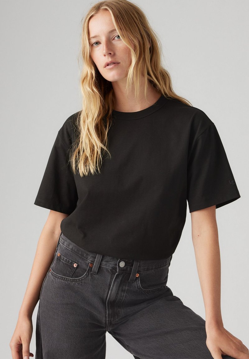 Svart t-skjorte med kort erm og rund hals, laget av bomull, brukt sammen med mørkegrå høyhalsede denimjeans med kobberdetaljer.
