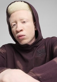 Felpa bordeaux con una finitura testurizzata, dotata di un piccolo logo Puma in rilievo sul petto e di un cappuccio regolabile con lacci. Composizione in tessuto morbido.