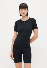 Zwart T-shirt met korte mouwen, ronde hals en raglanmouwen. Aansluitend ontwerp met een zachte textuur, gecombineerd met zwarte fietsshorts.