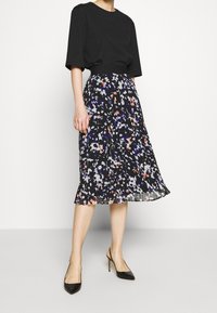 Černý top s krátkými rukávy spojený s volnou sukni délky ke kolenům s barevným květinovým vzorem na černém pozadí. Černé podpatky.