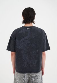 Sort oversized t-shirt med et mørkt dragegrafik på ryggen. Lavet af blødt bomuld med en afslappet pasform og korte ærmer.