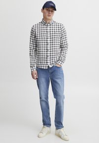 Knappe skjorte i svart og hvitt rutemønster, parret med lyseblå jeans og kremfargede sneakers. Blå caps fullfører antrekket.