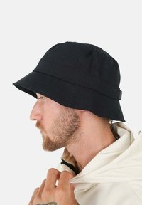 Czarna czapka typu bucket z szerokim rondem, wykonana z materiału, z wentylacyjnymi oczkami i regulowanym paskiem z tyłu.