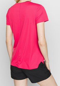 Kurzes, ärmelloses, pinkes Sportshirt aus strukturiertem Material mit Rundhalsausschnitt und belüfteten Seiten, kombiniert mit schwarzen Shorts.