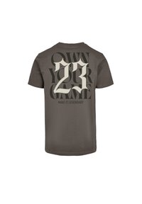 Mørk grå T-shirt lavet af bomuld, med fedt cremefarvet og sort grafisk tekst: "OWN YOUR GAME" og "23" på ryggen.