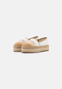Espadrilles beige et blanches avec tige en toile, semelle en jute tressé et bout arrondi. Détails de couture subtils sur la tige.