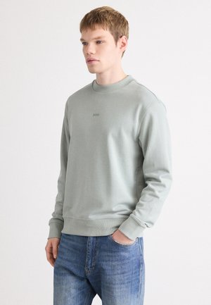Light green sweatshirt with a crew neck and ribbed cuffs, featuring a subtle logo on the chest, paired with blue jeans. Soft fabric texture.