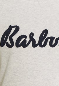 Světlá šedá tkanina s tmavě modrým vyšitým textem "Barbour." Košile má kulatý výstřih a hladkou texturu.