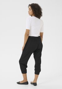 Pantalons jogger noirs à taille élastique avec poignets, associés à un haut ajusté blanc. Texture lisse, design simple, style décontracté.