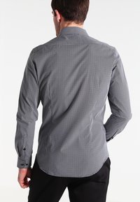 Musta-valkoinen kuvioitu kauluspaita, jossa on napillinen kaulus, pitkät hihat ja mustat napit. Sileä kangaspinta ja räätälöity istuvuus.