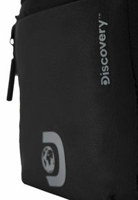 Borsa in tessuto nero con finitura texturizzata. Presenta un logo grigio "Discovery" e un design a globo. Include una chiusura a zip e un'asola laterale.