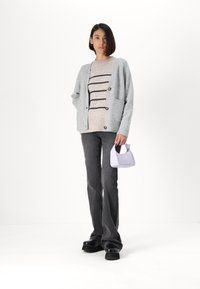Gray knit cardigan with buttons, layered over a beige striped sweater. Black flared jeans and a small lilac handbag complete the outfit.