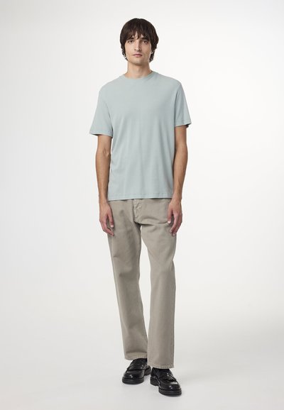 T-shirt di cotone azzurro chiaro, con scollo a giro e maniche corte, abbinato a pantaloni beige a gamba dritta e scarpe nere con dettagli testurizzati.