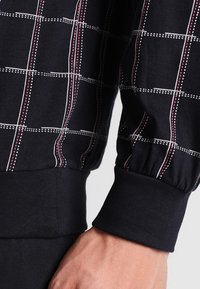 Zwarte pullover met een ruitpatroon in rood en wit. Geribbelde manchetten; zachte stof met een lichte glans. Klassieke pasvorm en afgeronde zoom.
