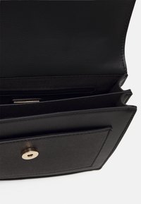 Černá kožená kabelka s texturovaným povrchem, vybavená zlatým zapínáním na cvok, otevřenými přihrádkami a vnitřní kapsou na zip.