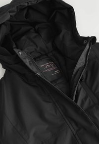 Veste à capuche noire avec fermeture éclair visible et étiquette indiquant Unlimited Tec vêtements haute performance, fabriqués au Myanmar.
