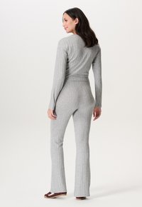 Graues geripptes Strickset mit langen Ärmeln und weit geschnittenen Hosen. Es bietet eine figurbetonte Silhouette und kontrastierende braune Akzente bei den Schuhen.