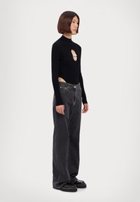 Schwarzer gerippter Langarm-Bodysuit mit seitlichen Ausschnitten und Perlenakzenten; kombiniert mit lockeren schwarzen Jeans und klobigen schwarzen Schuhen.