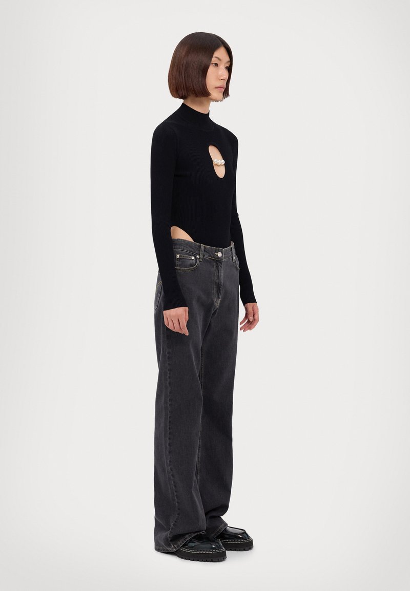 Schwarzer gerippter Langarm-Bodysuit mit seitlichen Ausschnitten und Perlenakzenten; kombiniert mit lockeren schwarzen Jeans und klobigen schwarzen Schuhen.