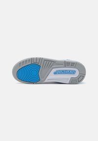 Suela de zapato con una base gris, detalle circular azul y patrones de agarre texturizados. Notable logo "JORDAN" en blanco sobre el fondo gris.