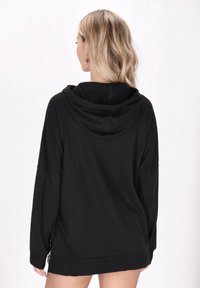 Felpa nera con cappuccio, caratterizzata da un motivo testurizzato a coste, con una vestibilità ampia e maniche lunghe, che enfatizza la semplicità nel design.