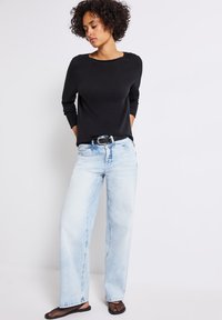 Svart långärmad topp, ljusblå vida jeans och svarta nät slip-on skor. Funktioner inkluderar en rund halslinje och bälte.