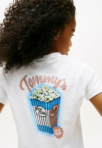 Hvid kort�ærmet t-shirt med et farverigt popcorn grafik og teksten "Tommy's", "POP CORN" og "HOT & FRESH." Blødt stof, afslappet pasform.