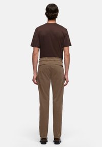 Bruine korte mouw t-shirt gecombineerd met beige geweven broek met achterzakken en een slanke pasvorm, gezien van achteren.