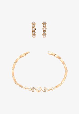 Kultainen rannekoru, jossa on yhdistettyjä suorakulmaisia osia ja kaareva keskiosa, jossa on upotettuja timantteja, yhdistettynä kultakorvakoruihin, joissa on helmiä ja timantteja.