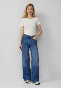 Witte geribbelde t-shirt met korte mouwen, gecombineerd met hoogwaist blauwe denim flared jeans. De jeans hebben een klassiek vijf-pocket ontwerp en een subtiele wassing.